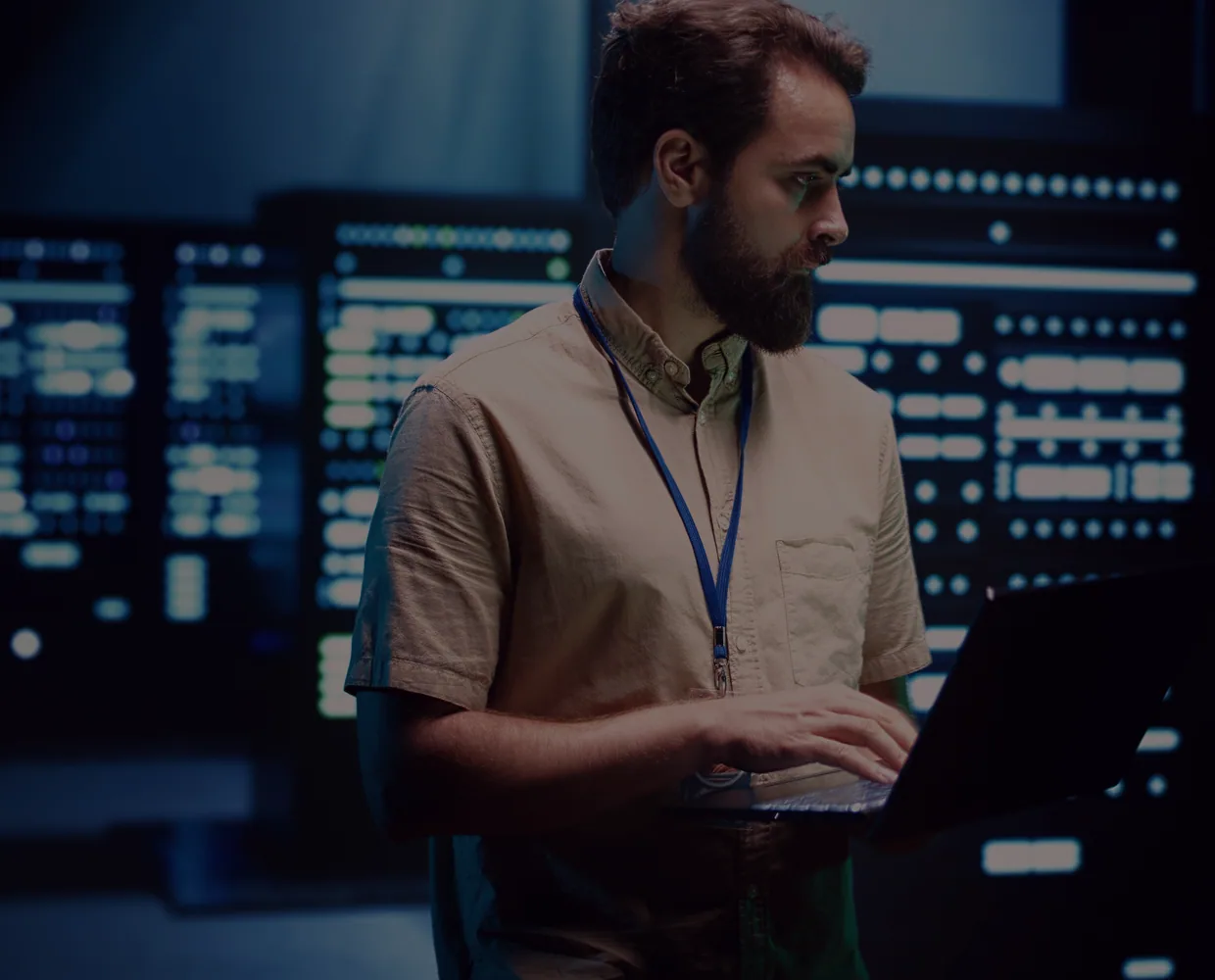 An engineer works at a laptop in front of lit server racks.