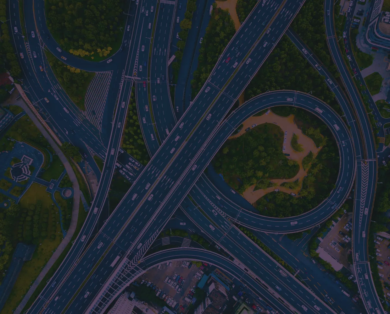 An aerial view of a motorway interchange, its roads weaving through green ground.